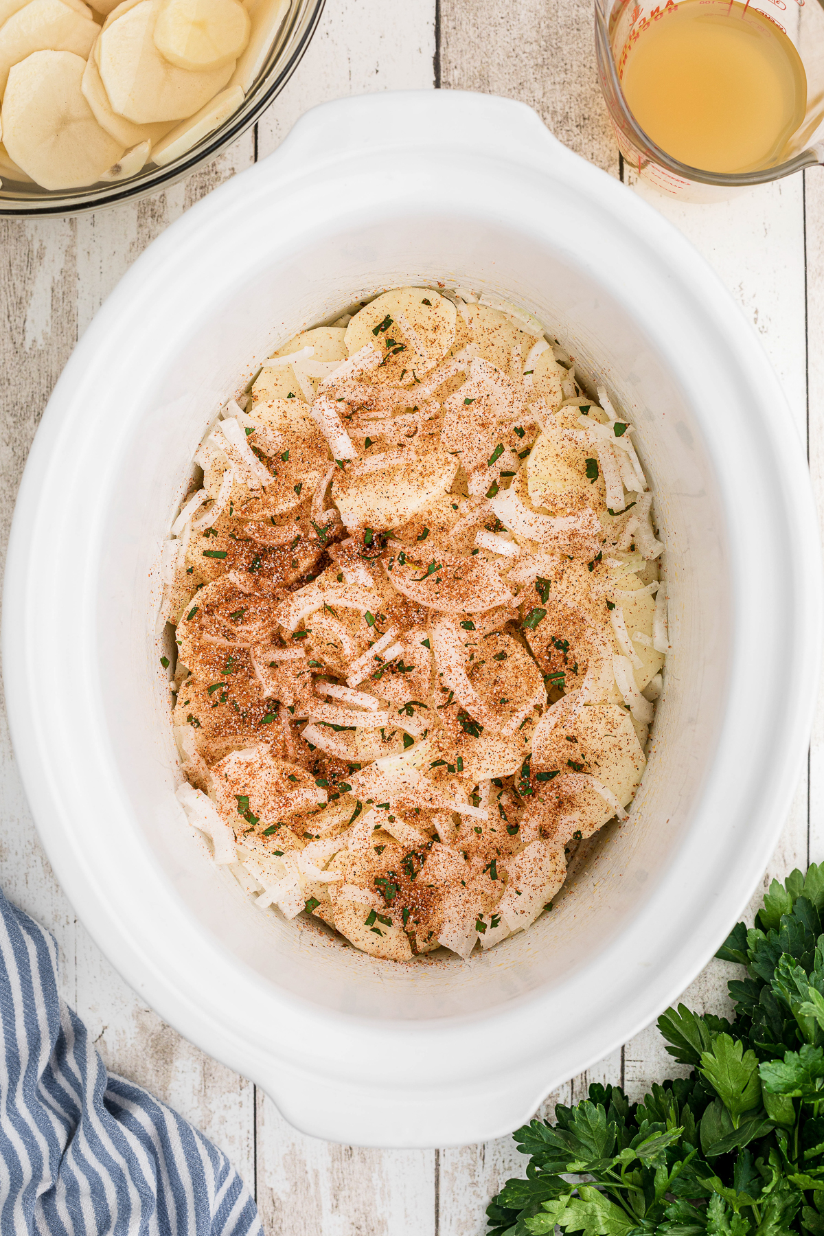 potatoes and onions in a slo cooker with seasonings on top.
