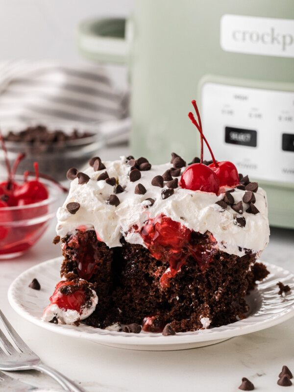 A slice of black forest cake on a plate in front of a crockpot.