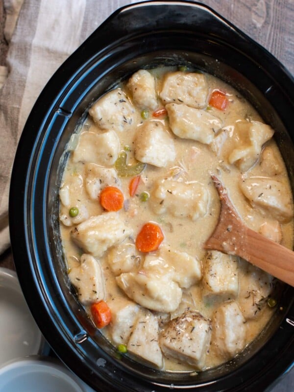 chicken and dumplings cooked in slow cooker with wooden spoon in it.