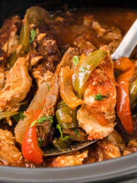 A spoon taking a scoop of fajita meat and veggies from a crockpot.