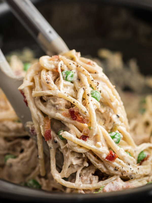 Slow cooker chicken carbonara being pulled up with tongs.