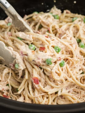 Tongs grabbing some slow cooker chicken carbonara from a crockpot.