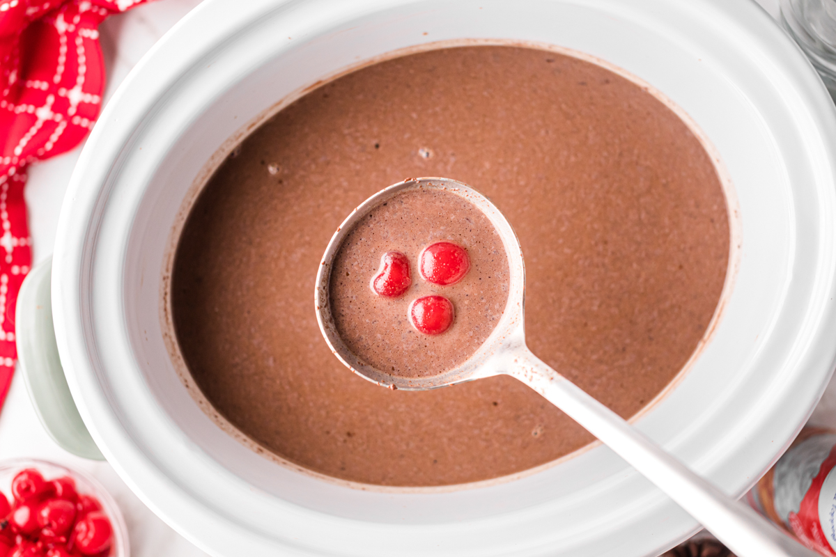 Slow cooker chocolate covered cherry hot chocolate with a ladle.