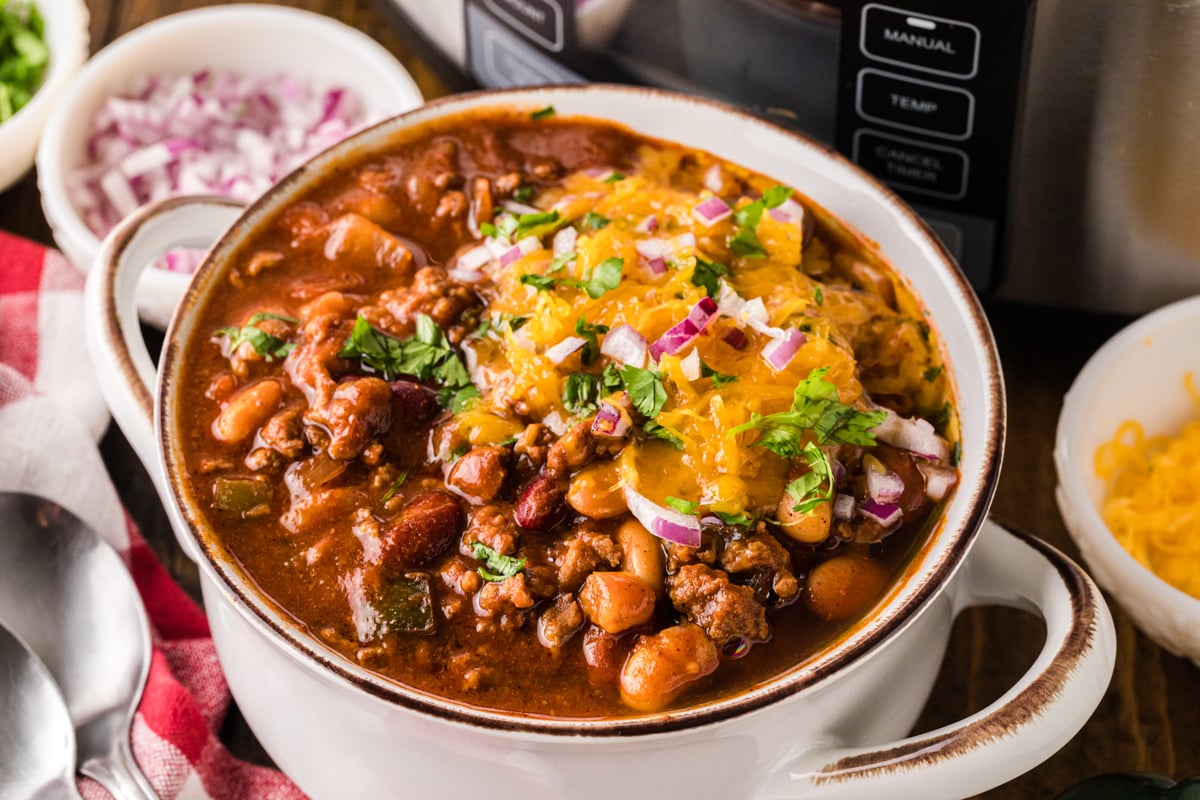 A bowl of chili topped with cheese, cilantro, and red onions.