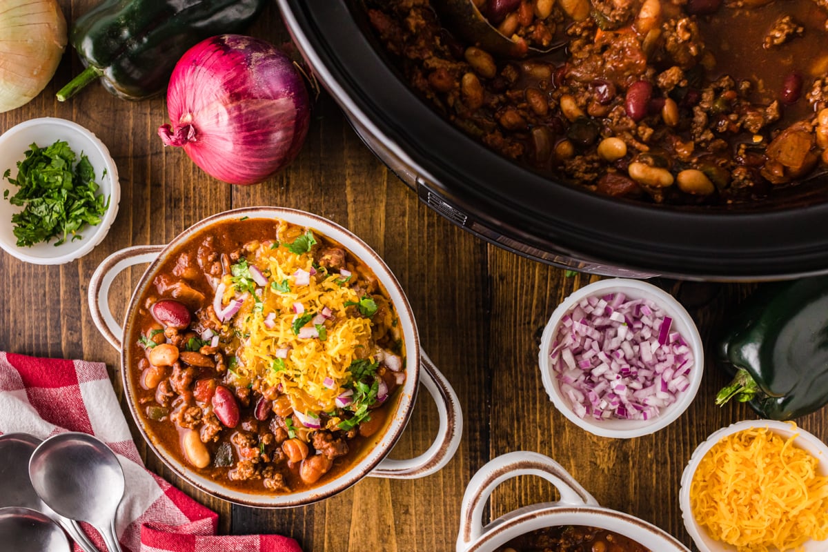 A bowl of chili in front of a crockpot with more chili.
