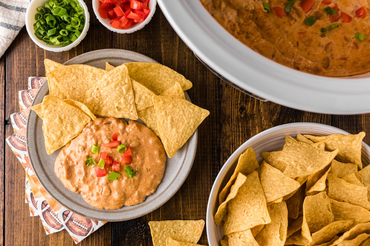 A plate of football dip and tortilla chips and some in a crockpot next to it.
