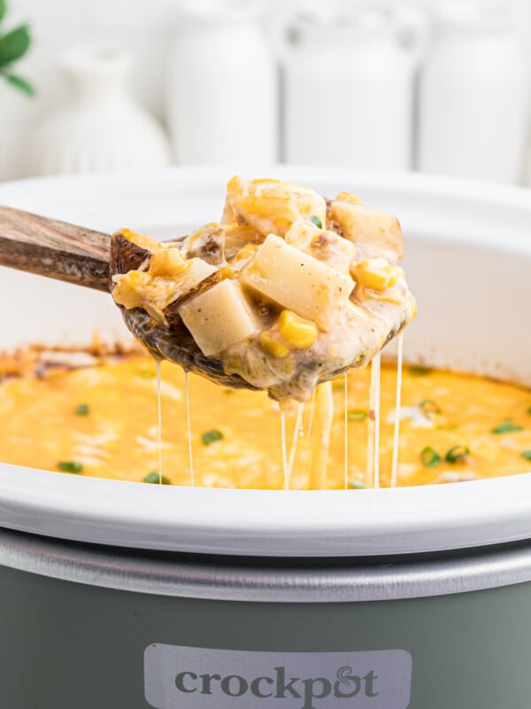 Scoop of hamburger hash on a wooden spoon coming from a slow cooker.