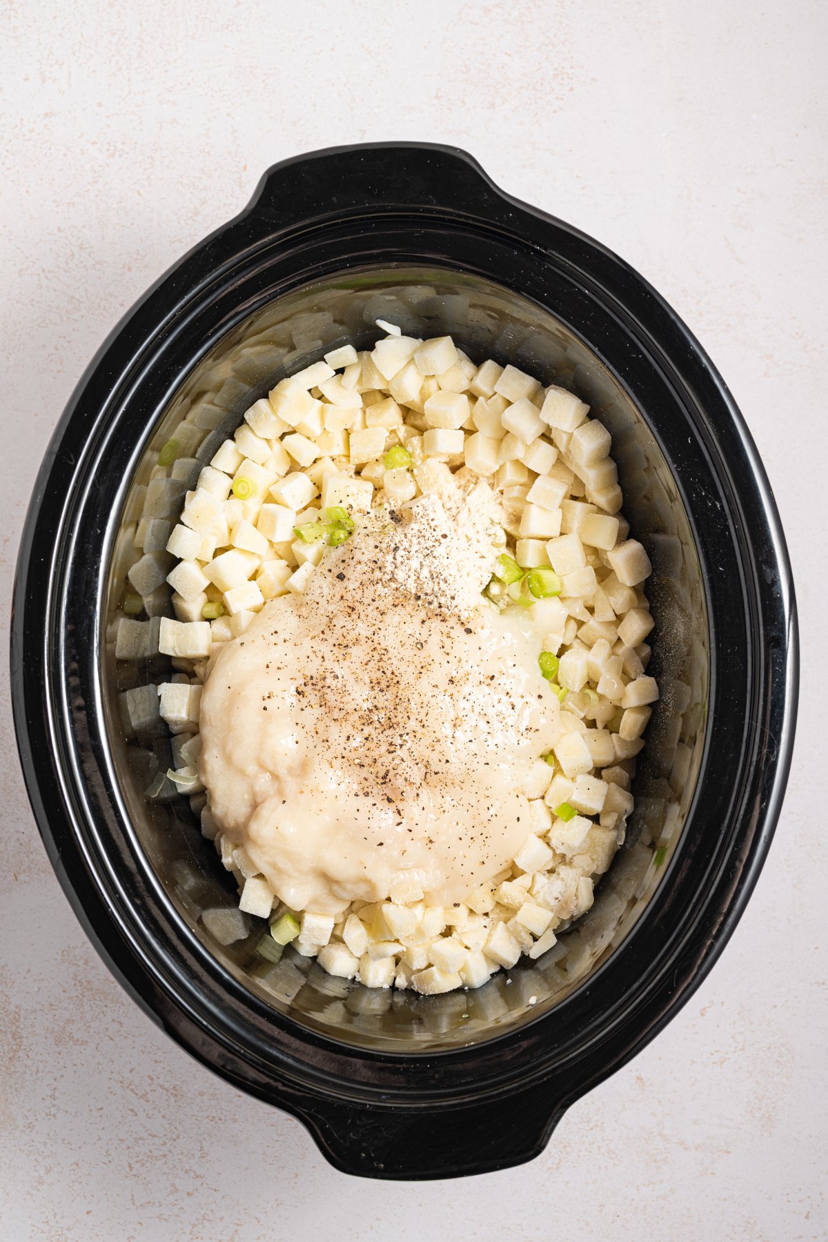 Cream soup and seasonings on top of potatoes and green onions in a crockpot.
