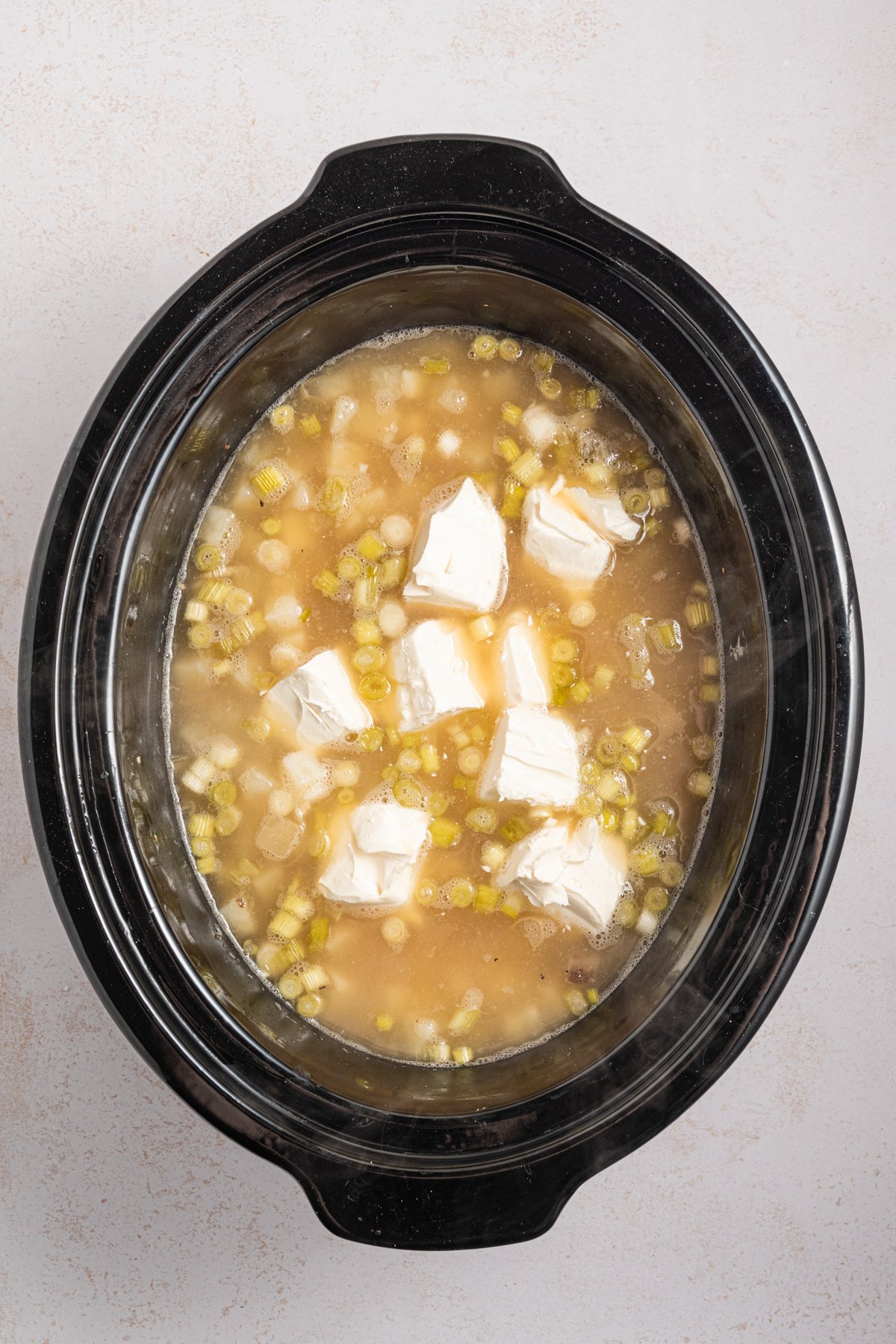 Cream cheese and chicken stock added to a crockpot.