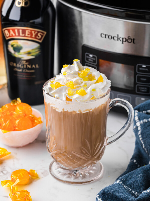 A mug of hot buttered rum in front of a slow cooker.