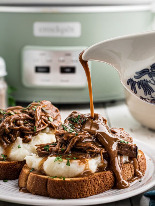 Gravy being poured over roast beef, mashed potatoes and toast.
