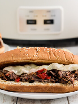 2 Italian beef sandwiches in front of a slow cooker.