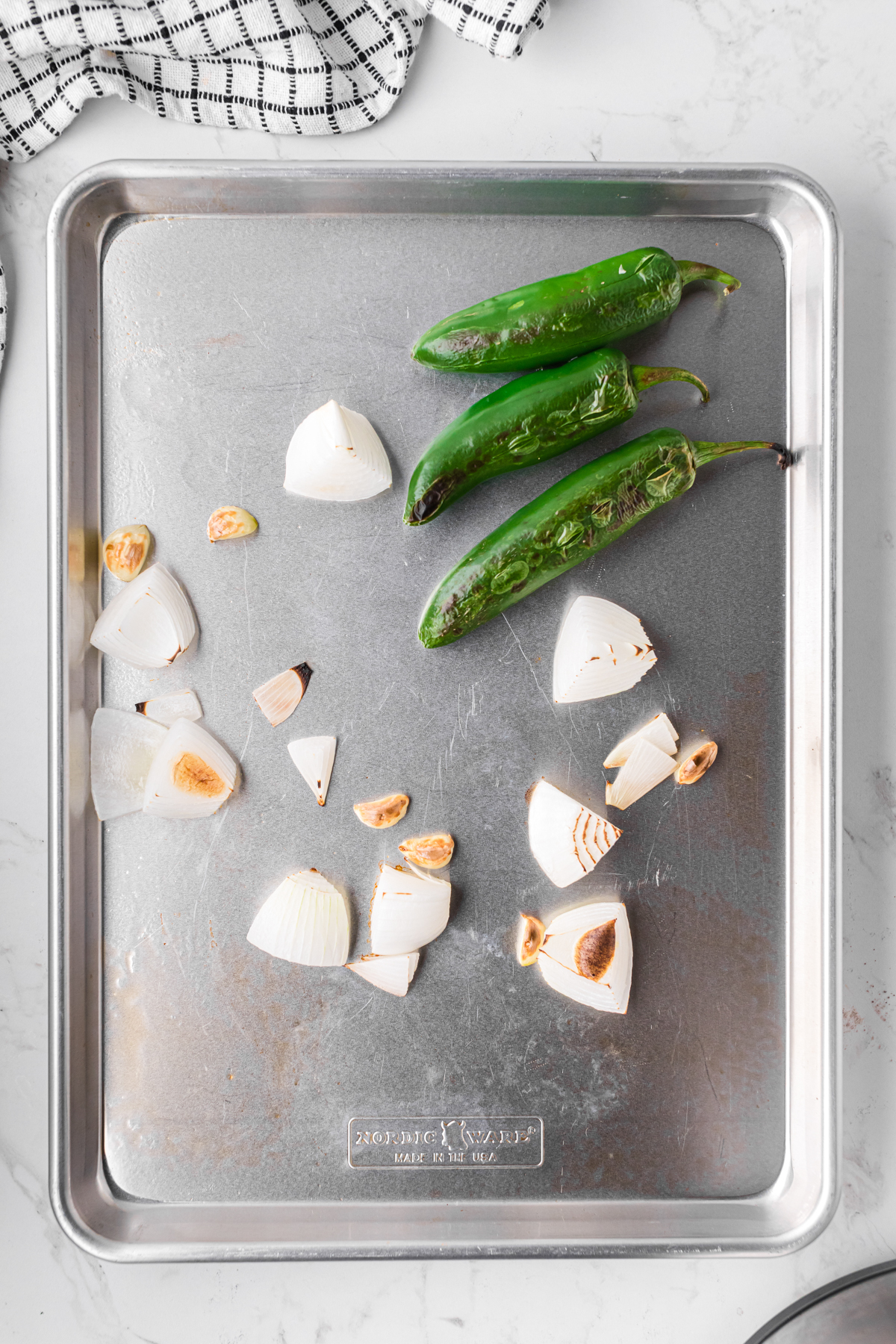 jalapenos, onion, and garlic on a baking sheet after broiling.