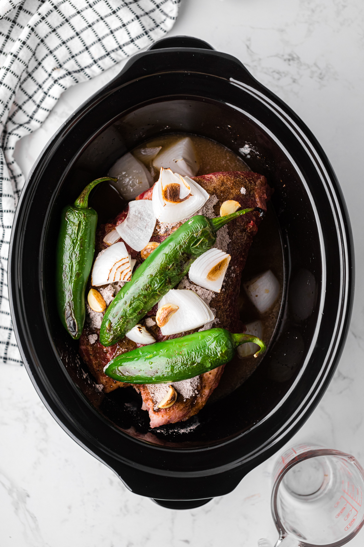 Broiled jalapenos, onion, and garlic added to beef in a slow cooker.