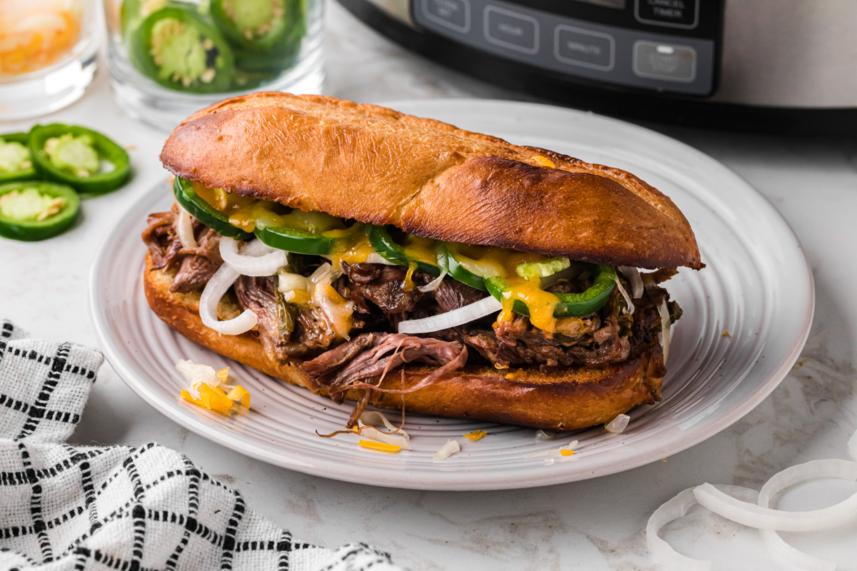 One of the slow cooker jalapeno beef sammies on a white plate in front of a crockpot.