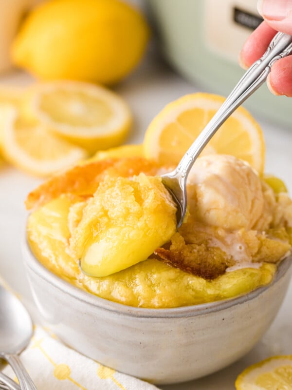 A hand holding a spoon taking a scoop of lemon dump cake from a bowl.
