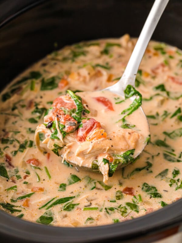 A ladle of mama leone's chicken soup coming out of a crockpot.