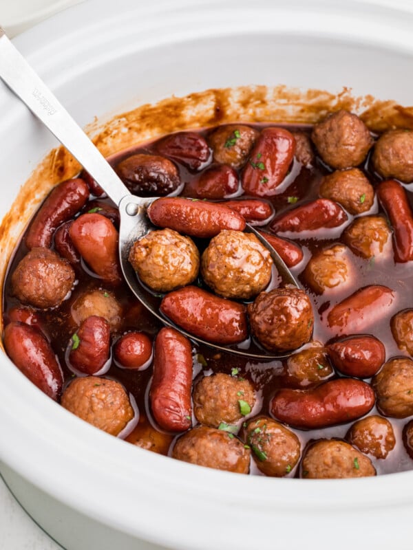 close up of meatballs and little smokies in a white slow cooker.
