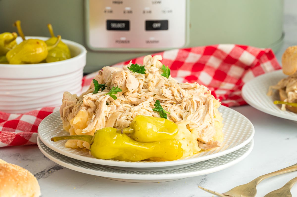 slow cooker mississippi chicken on a stack of white plates.