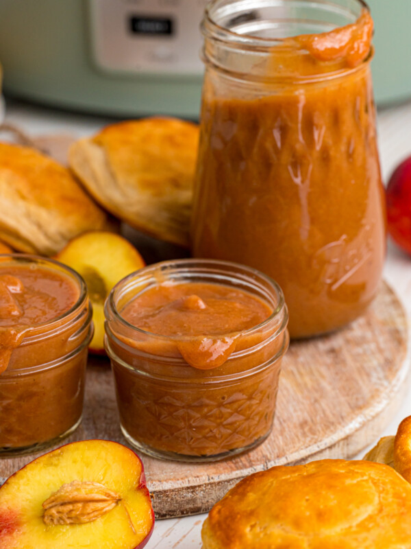Jars of peach butter in front of a crockpot.