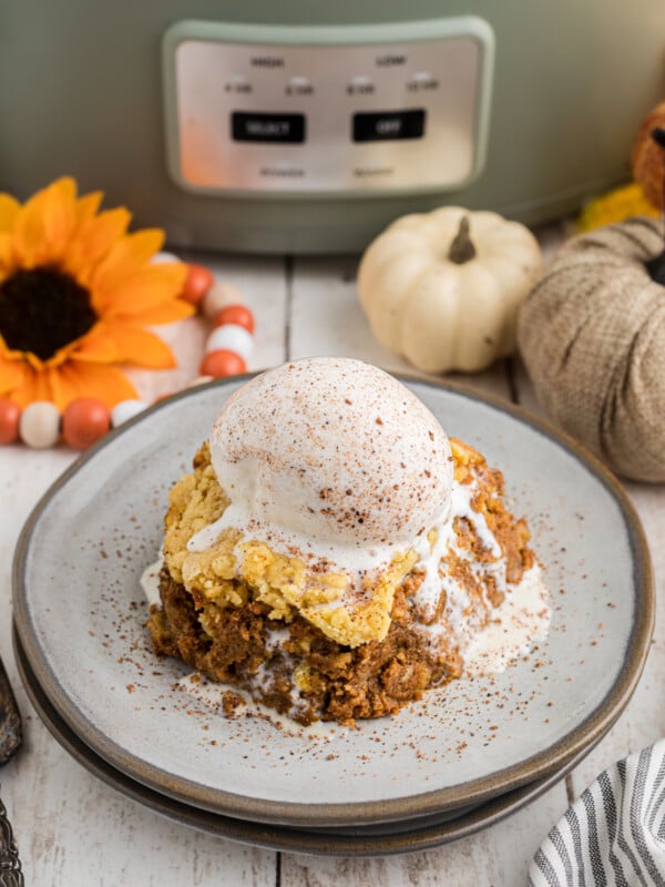 Slice of slow cooker pumpkin cobbler with ice cream on top on a plate.