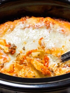 close up of ravioli in slow cooker with metal spoon in it.