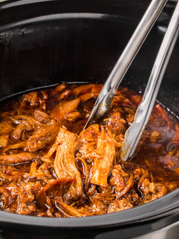 root beer pulled pork in a slow cooker with tongs.