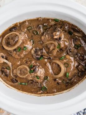 salsibury steak patties in a slow cooker with gravy and onions.
